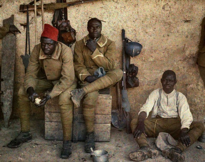 Three Senegalese soldiers in uniform, including red caps, resting between fighting.